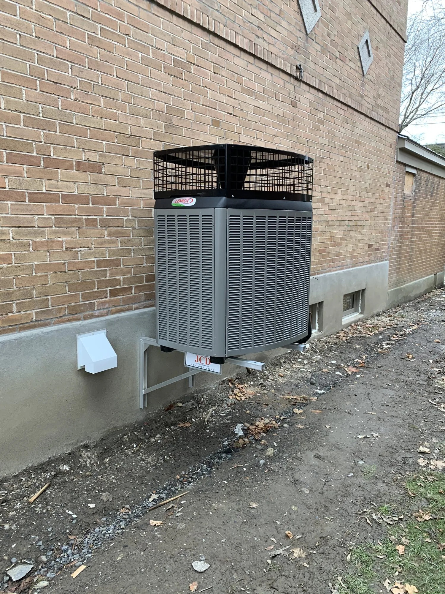 A Lennox heat pump outdoor unit on a wall bracket beside a brick house
